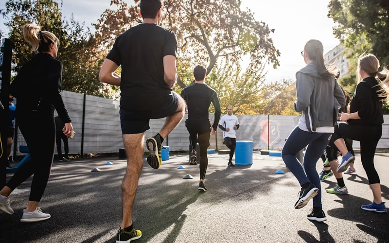 Group of people outside, standing in a circle, jogging in place as a warm-up before running.