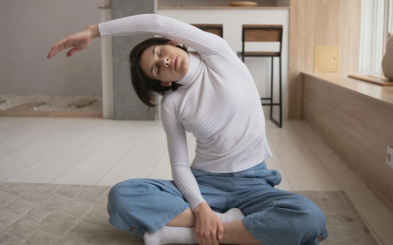 Adult seated on the floor on a rug in an office stretching arm over head.