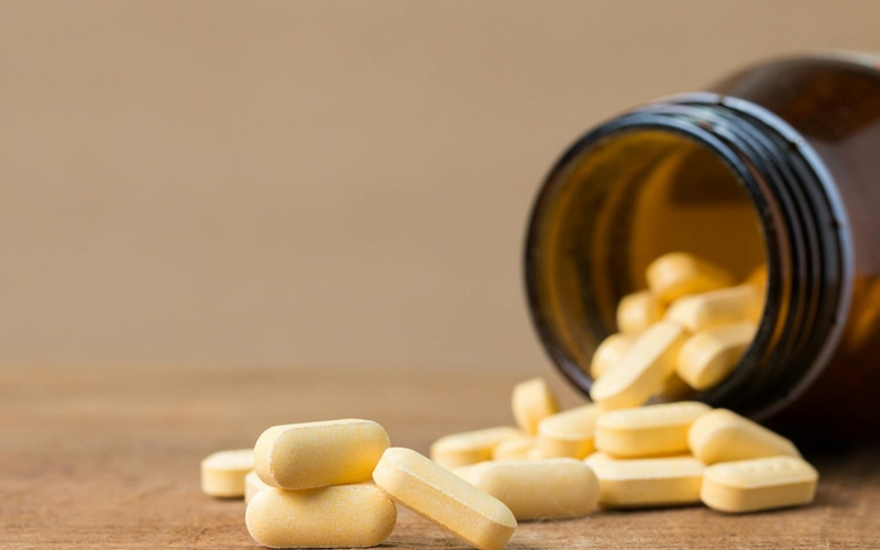 Yellow tablets spilling out of a brown bottle onto a table.