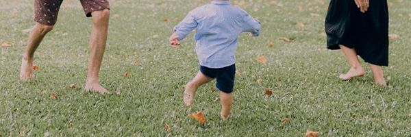 Two adults and a child dance barefoot in the grass.