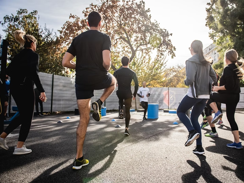 Group of people outside, standing in a circle, jogging in place as a warm-up before running.