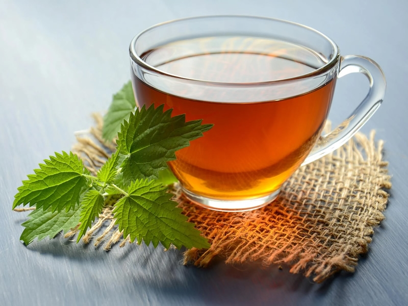 Clear glass teacup with amber tea on a burlap coaster with a green peppermint leaf beside the teacup.