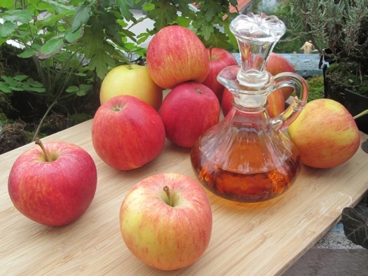 Red apples and decanter of vinegar on a wood table in a garden.