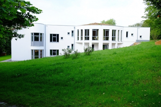 White clinic building with large windows surrounded by green grass.