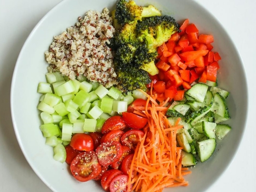 Diced tomatoes, celery, broccoli, red peppers, and cucumbers with shredded carrots and loose grains on a plate.