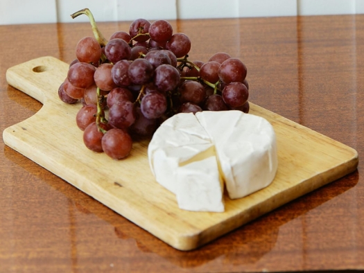 Wood board with red grapes and wheel of white cheese.