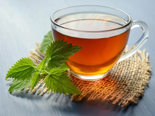 Clear glass teacup with hot tea on a burlap coaster next to a sprig of green mint leaves.