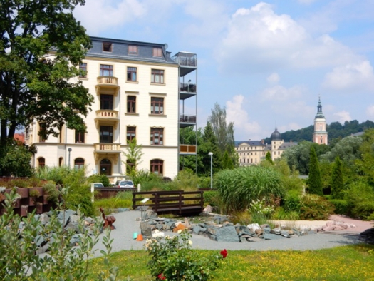 4-story light tan building with balconies and gardens