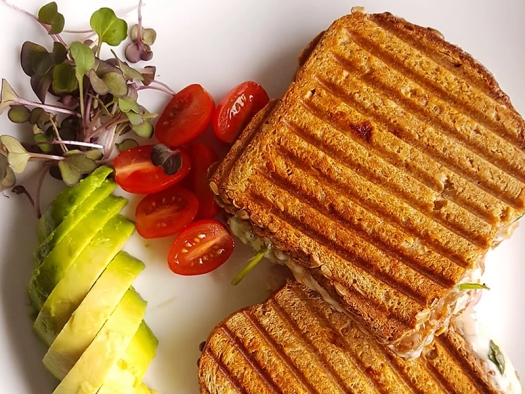 grilled cheese sandwich on plate with tomatoes and avocado slices on the side