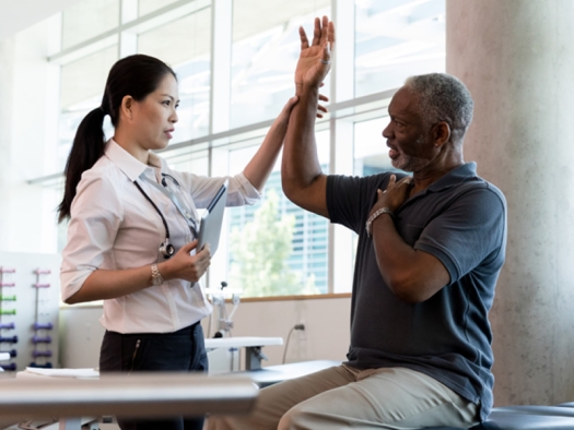 female doctor testing male patent seated on table with arm raised