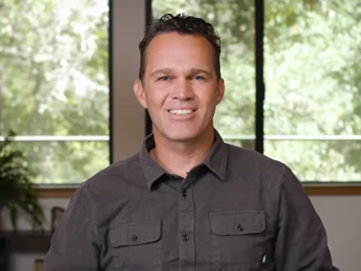 Screenshot from video: Zach Bush seated in front of window with trees in background