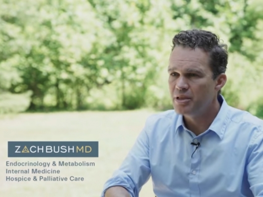 Dr. Zach Bush, young white male in blue shirt, sitting in chair with background of trees and field