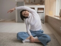 Adult seated on the floor on a rug in an office stretching arm over head.