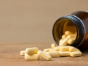 Yellow tablets spilling out of a brown bottle onto a table.